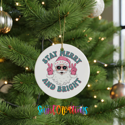 Round ceramic Christmas ornament featuring Santa in sunglasses giving peace signs with Stay Merry and Bright lettering, hanging on a green Christmas tree