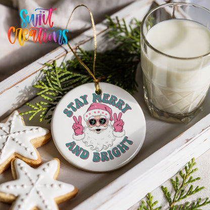 Round ceramic Christmas ornament featuring Santa in sunglasses giving peace signs with Stay Merry and Bright lettering, styled with cookies and milk