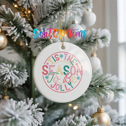 Round ceramic Christmas ornament featuring round pastel ’Tis the Season to Be Jolly holiday typography, hanging on a frosted Christmas tree