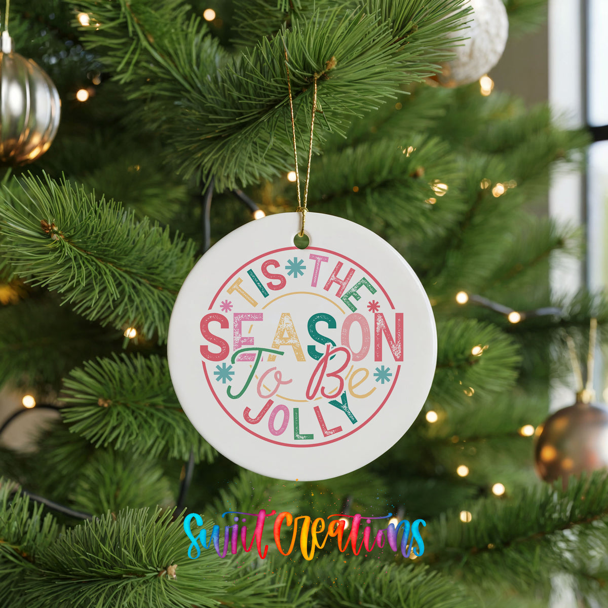 Round ceramic Christmas ornament featuring round pastel ’Tis the Season to Be Jolly holiday typography, hanging on a green Christmas tree
