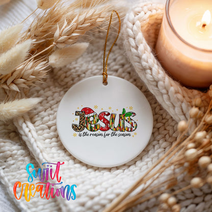 Round ceramic Christmas ornament featuring colorful Jesus Is the Reason for the Season typography, styled beside a candle and cozy knit blanket
