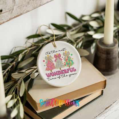 Round ceramic Christmas ornament featuring It’s the Most Wonderful Time of the Year lettering with colorful gifts and trees, styled on books with holiday greenery