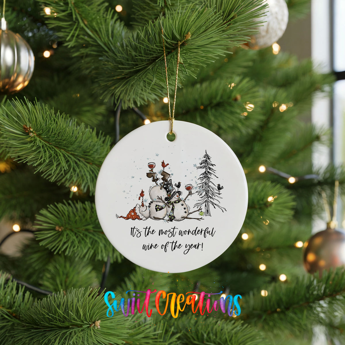 Round ceramic Christmas ornament featuring tipsy snowmen with wine glasses and It’s the Most Wonderful Wine of the Year lettering, hanging on a green Christmas tree
