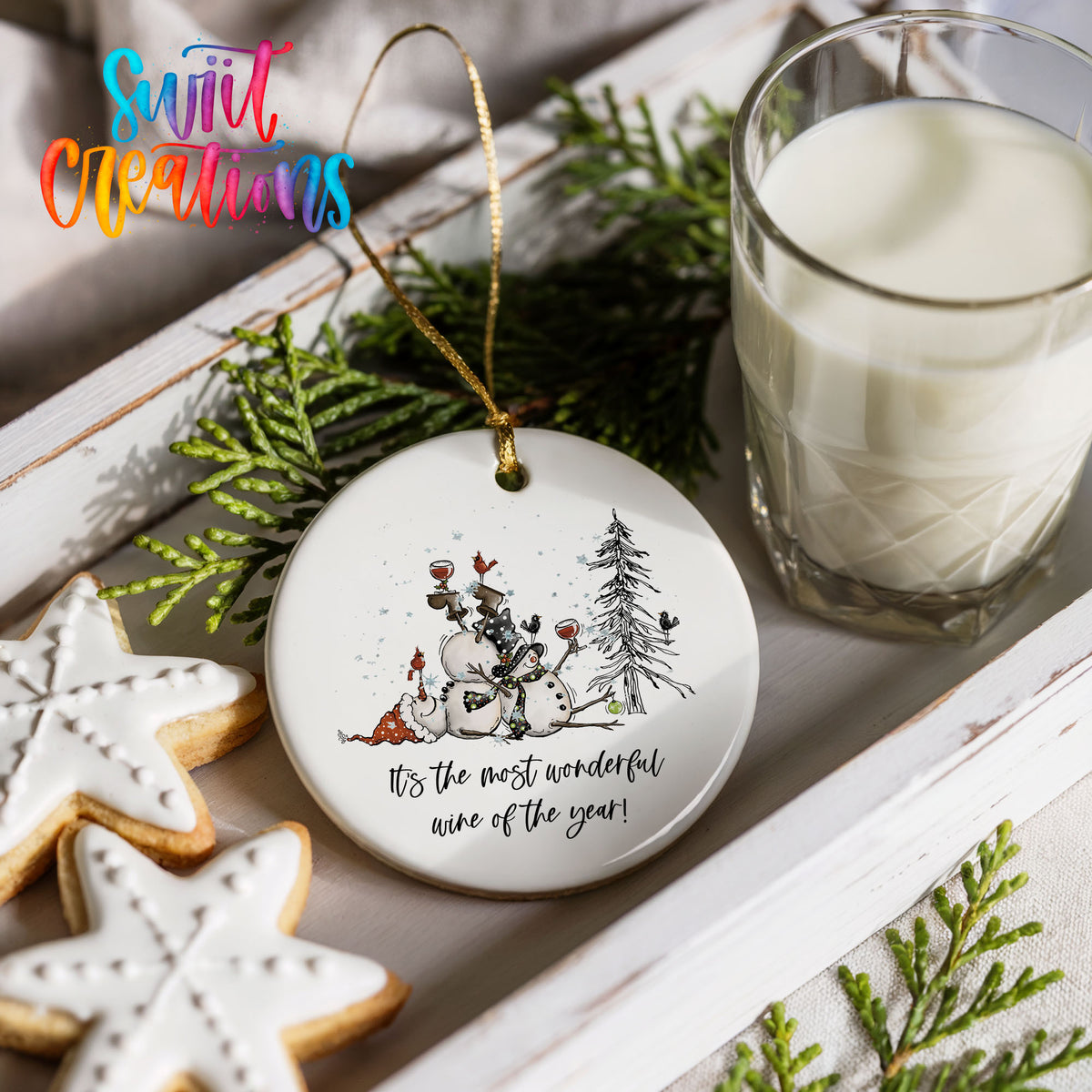 Round ceramic Christmas ornament featuring tipsy snowmen with wine glasses and It’s the Most Wonderful Wine of the Year lettering, styled with cookies and milk