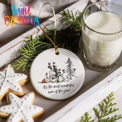 Round ceramic Christmas ornament featuring tipsy snowmen with wine glasses and It’s the Most Wonderful Wine of the Year lettering, styled with cookies and milk