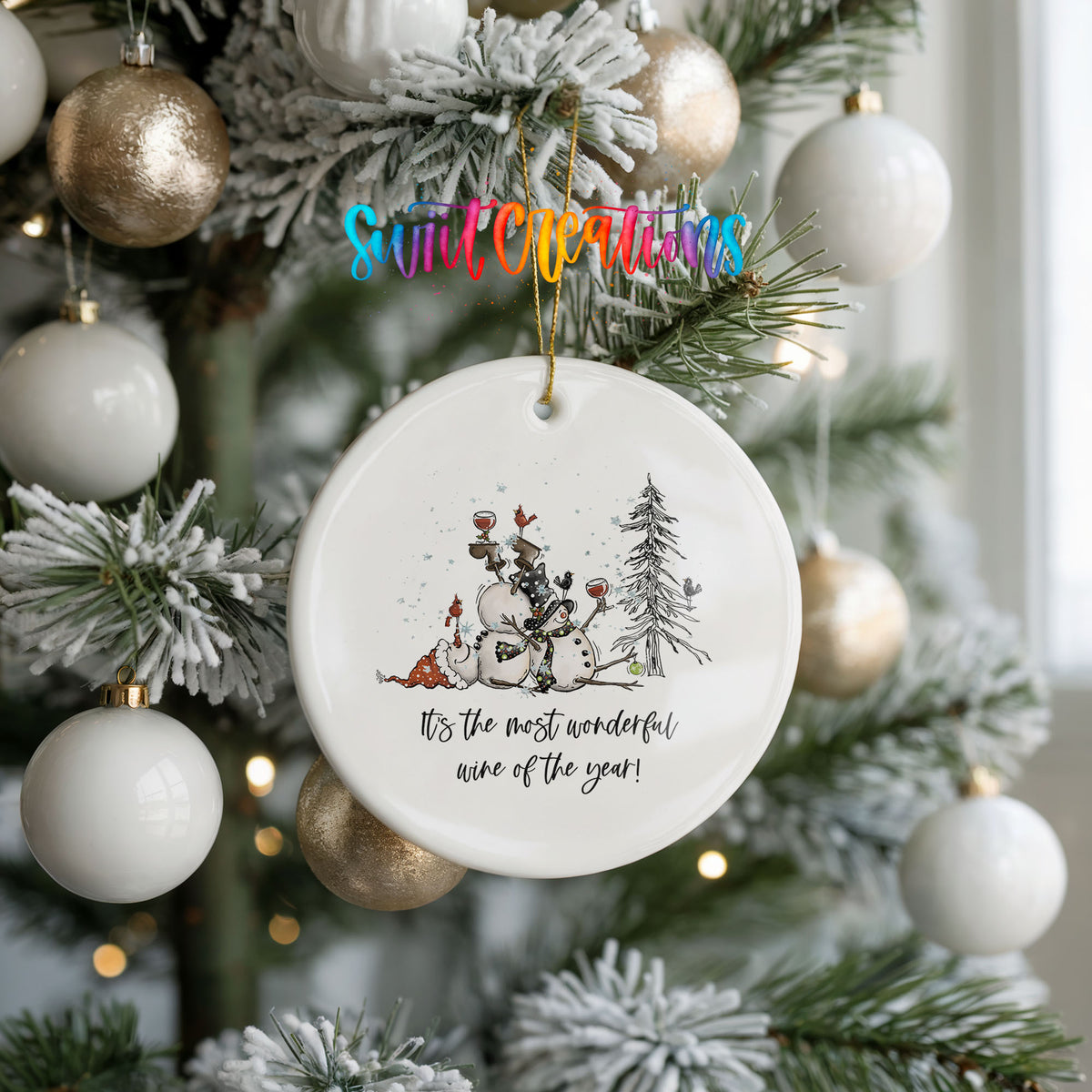 Round ceramic Christmas ornament featuring tipsy snowmen with wine glasses and It’s the Most Wonderful Wine of the Year lettering, hanging on a frosted holiday tree