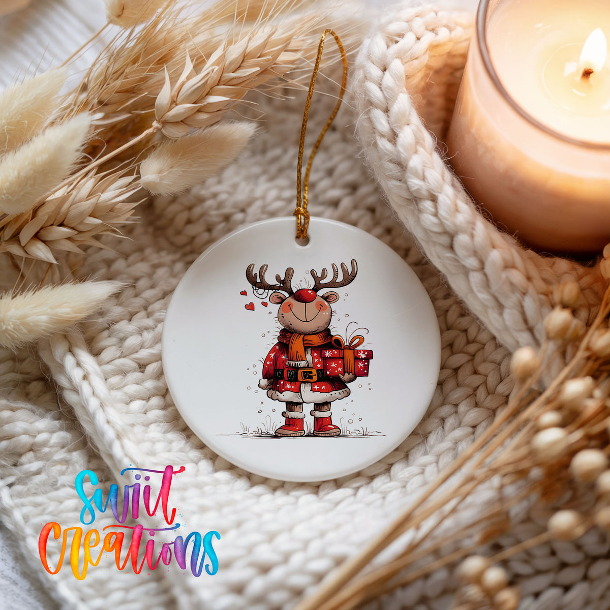 Round ceramic Christmas ornament featuring cheerful reindeer in a Santa suit holding wrapped Christmas gifts, styled beside a candle and cozy knit blanket