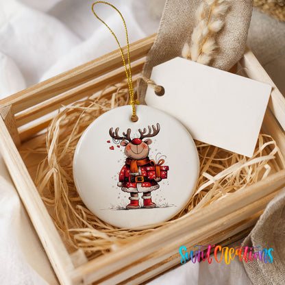 Round ceramic Christmas ornament featuring cheerful reindeer in a Santa suit holding wrapped Christmas gifts, presented in a rustic wooden gift crate