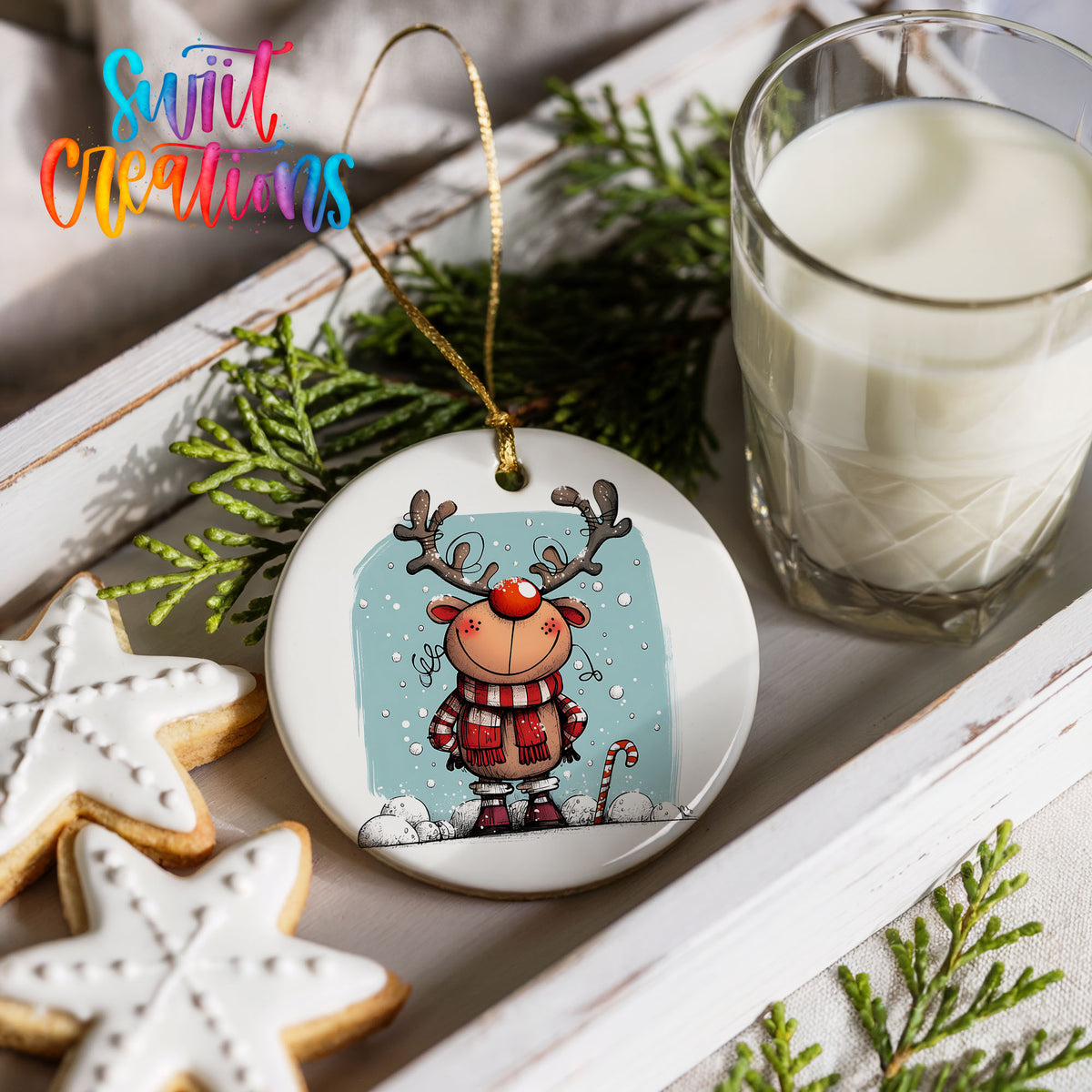 Round ceramic Christmas ornament featuring smiling reindeer in red plaid winter clothes against a snowy blue background, styled with cookies and milk