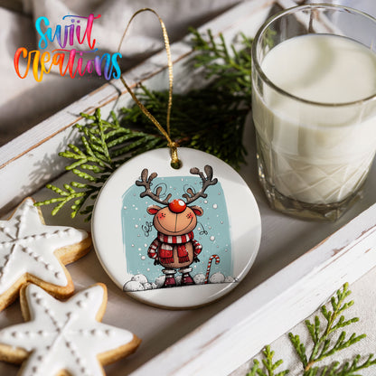 Round ceramic Christmas ornament featuring smiling reindeer in red plaid winter clothes against a snowy blue background, styled with cookies and milk