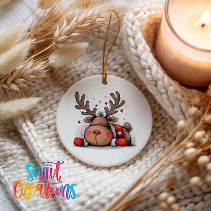 Cute Reindeer with Red Gift Bag Christmas ornament styled beside a candle and cozy knit blanket