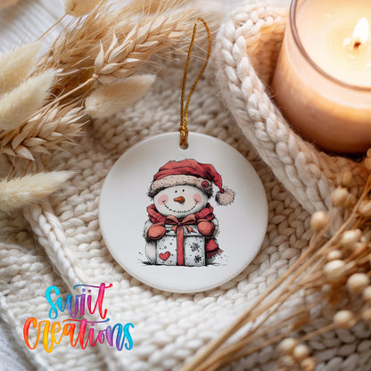 Snowman with Wrapped Christmas Gift Christmas ornament styled beside a candle and cozy knit blanket