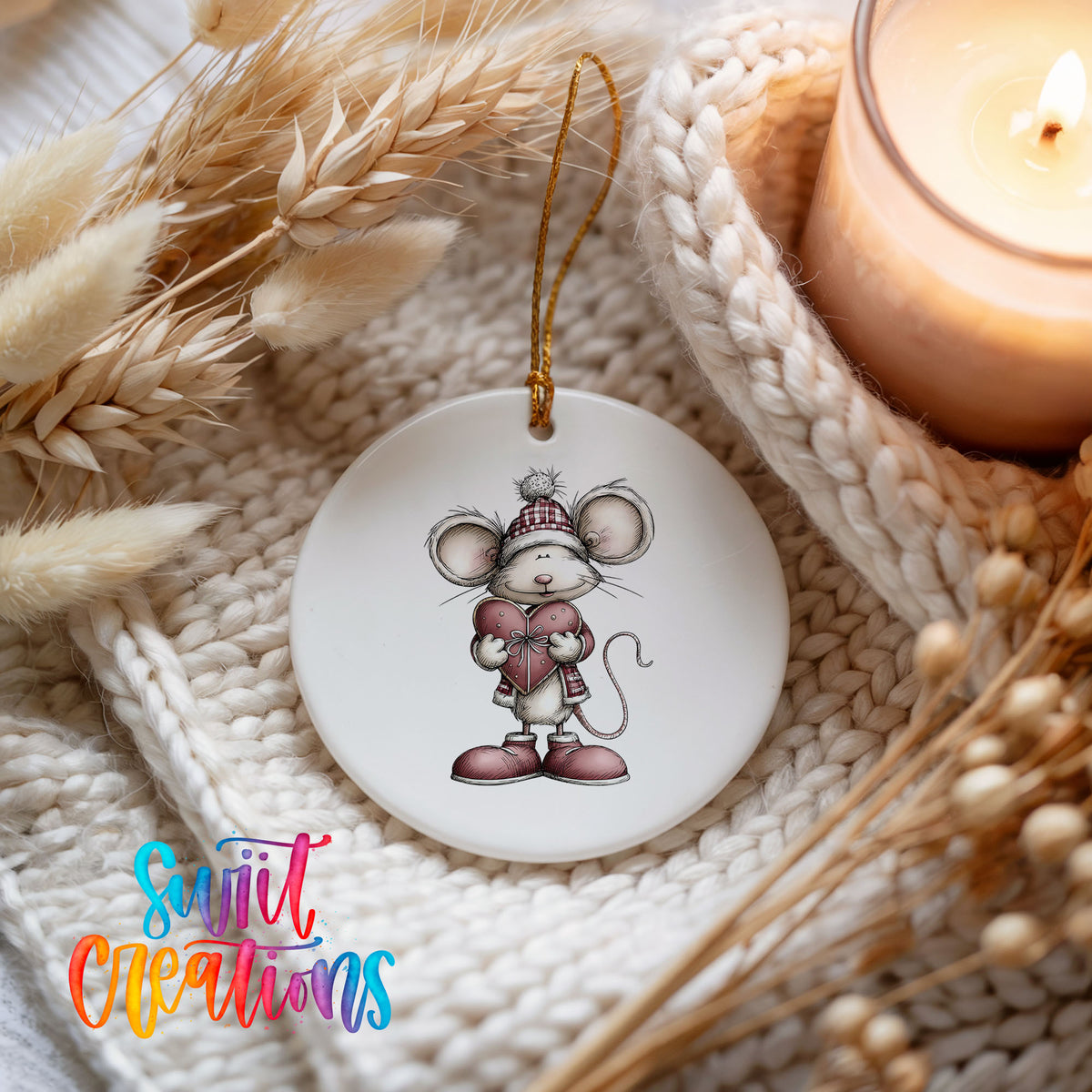 pink mouse holding a heart ceramic Christmas ornament styled on a cozy knit blanket