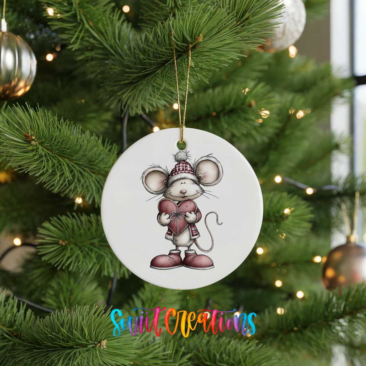 pink mouse holding a heart ceramic Christmas ornament hanging on a lit Christmas tree