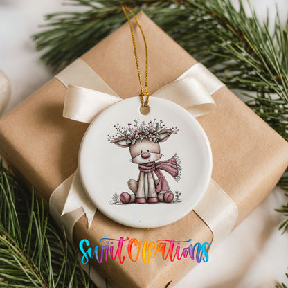 pink reindeer in a scarf with a berry antler crown ceramic Christmas ornament displayed on a wrapped Christmas gift