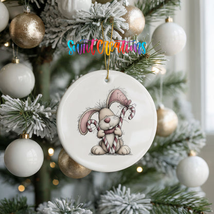 pink rabbit holding a candy cane ceramic Christmas ornament hanging on a frosted tree with ornaments