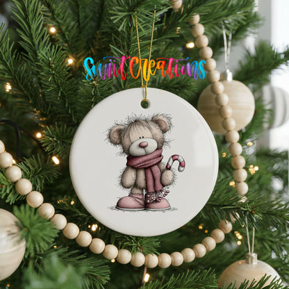 teddy bear in a pink scarf holding a candy cane ceramic Christmas ornament hanging on a green Christmas tree