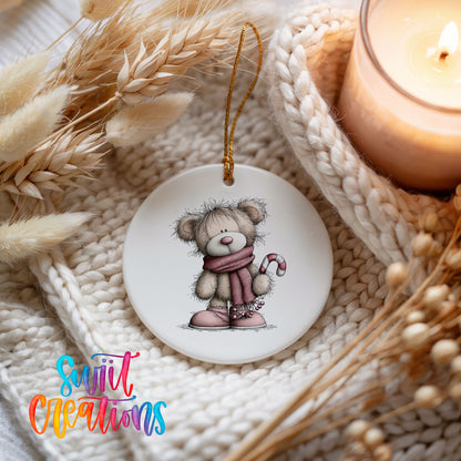 teddy bear in a pink scarf holding a candy cane ceramic Christmas ornament styled on a cozy knit blanket