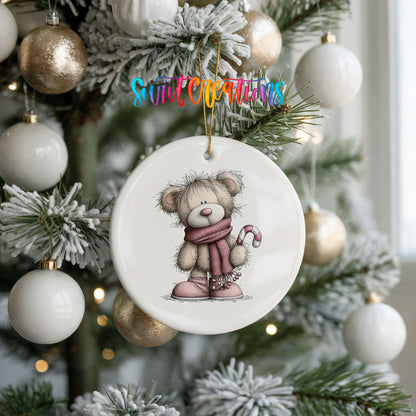 teddy bear in a pink scarf holding a candy cane ceramic Christmas ornament hanging on a frosted tree with ornaments