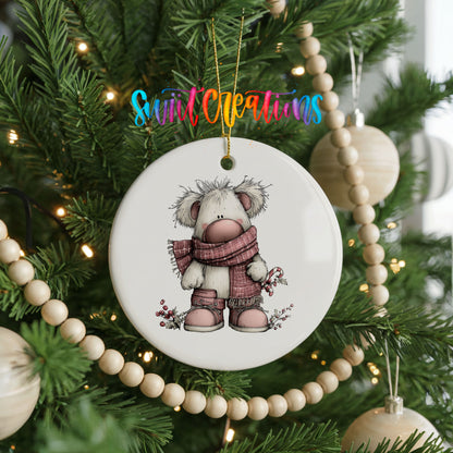 teddy bear in a pink winter sweater with holly ceramic Christmas ornament hanging on a green Christmas tree