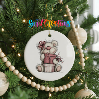 teddy bear sitting on a wrapped Christmas gift ceramic Christmas ornament hanging on a green Christmas tree