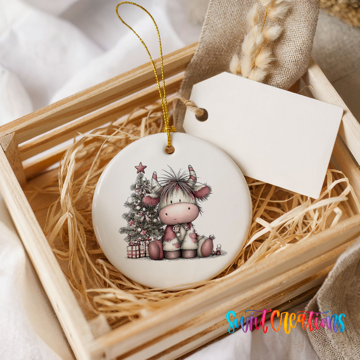 Highland cow beside a decorated Christmas tree and gifts ceramic Christmas ornament displayed in a wooden gift crate
