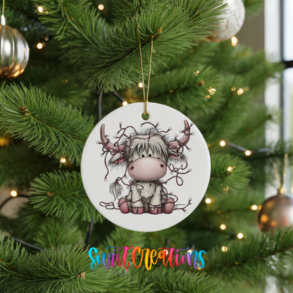 Highland cow with decorated antlers and Christmas lights ceramic Christmas ornament hanging on a lit Christmas tree