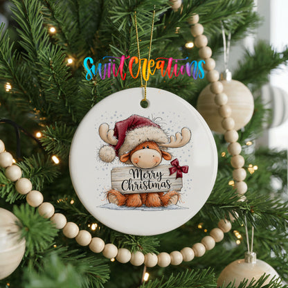 moose in a Santa hat holding a Merry Christmas sign ceramic Christmas ornament hanging on a green Christmas tree