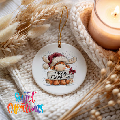 moose in a Santa hat holding a Merry Christmas sign ceramic Christmas ornament styled on a cozy knit blanket