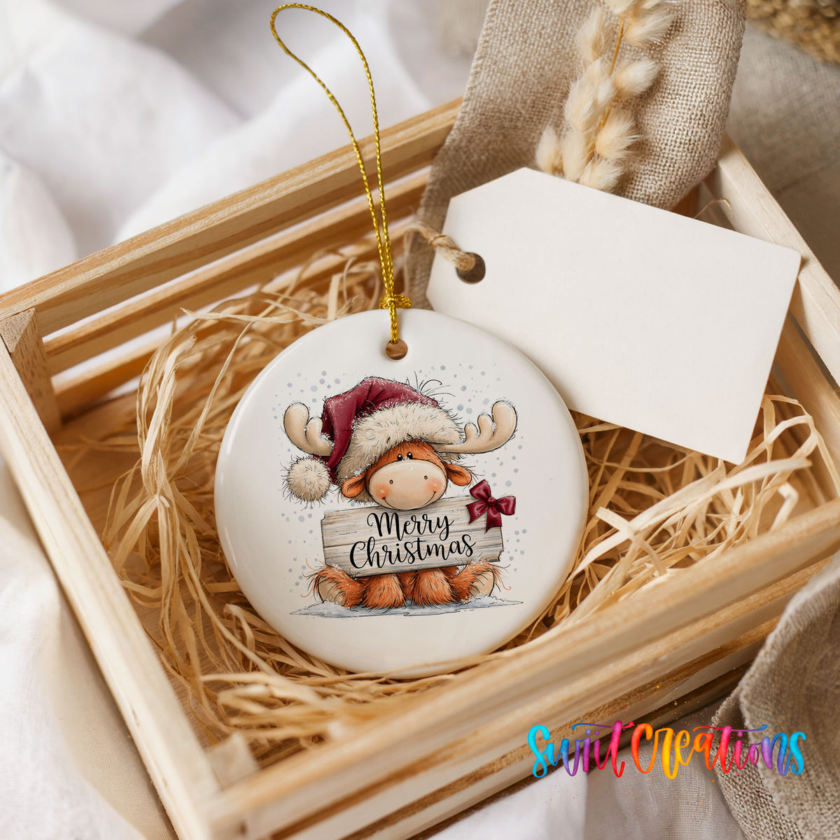 moose in a Santa hat holding a Merry Christmas sign ceramic Christmas ornament displayed in a wooden gift crate