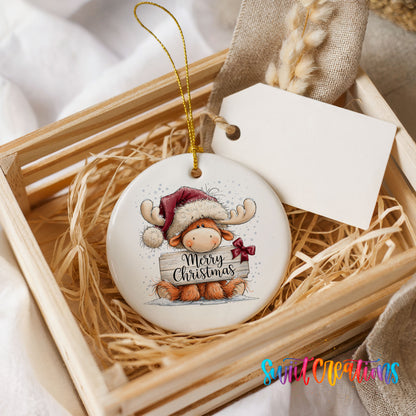 moose in a Santa hat holding a Merry Christmas sign ceramic Christmas ornament displayed in a wooden gift crate