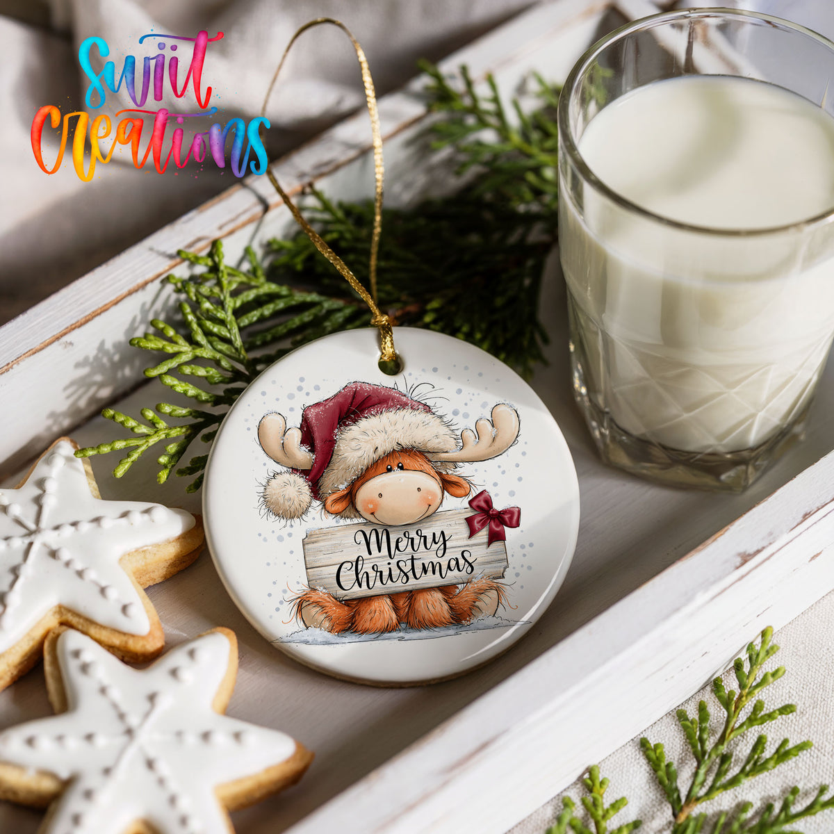 moose in a Santa hat holding a Merry Christmas sign ceramic Christmas ornament styled with holiday cookies and a candle