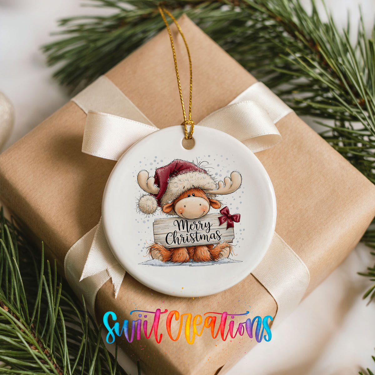 moose in a Santa hat holding a Merry Christmas sign ceramic Christmas ornament displayed on a wrapped Christmas gift