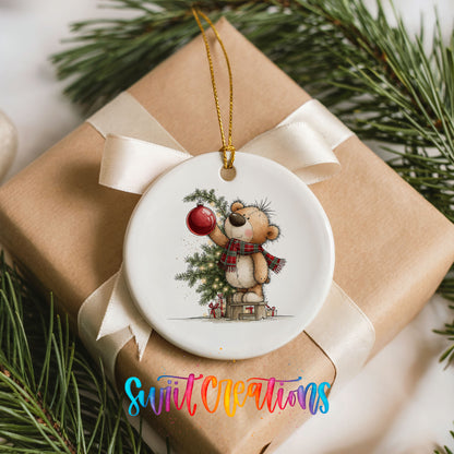 teddy bear holding a red ornament beside a Christmas tree ceramic Christmas ornament displayed on a wrapped Christmas gift