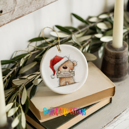 teddy bear in a Santa hat holding a Merry Christmas sign ceramic Christmas ornament styled on stacked books with greenery