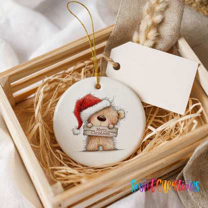 teddy bear in a Santa hat holding a Merry Christmas sign ceramic Christmas ornament displayed in a wooden gift crate