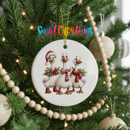 three Christmas geese wearing holiday wreaths ceramic Christmas ornament hanging on a green Christmas tree