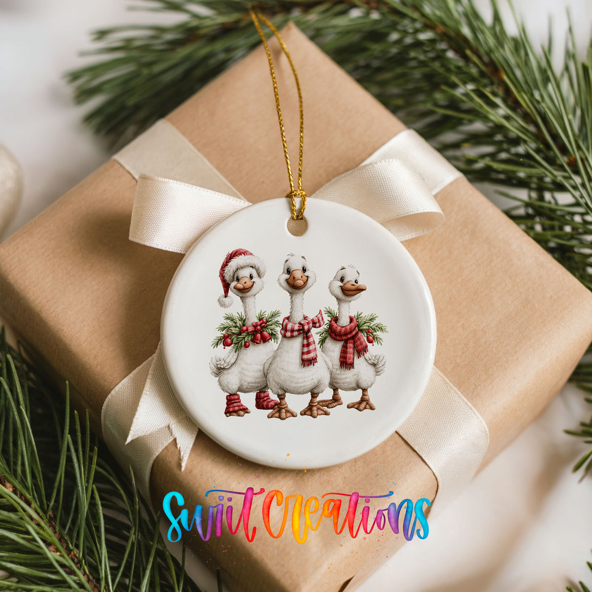 three Christmas geese wearing holiday wreaths ceramic Christmas ornament displayed on a wrapped Christmas gift