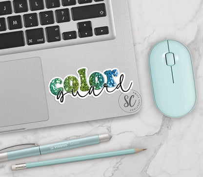 Green Glitter Color Guard vinyl sticker on a silver laptop next to a mint mouse and pens