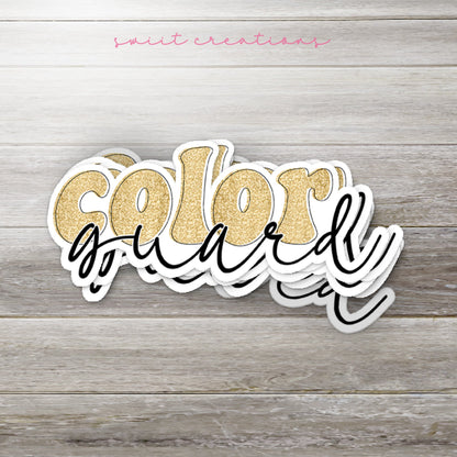 Stack of Gold Glitter Color Guard glossy stickers on a gray wood table