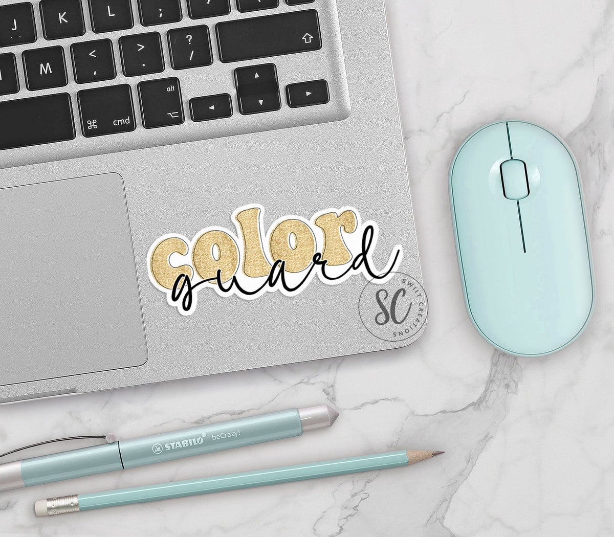 Gold Glitter Color Guard vinyl sticker on a silver laptop next to a mint mouse and pens