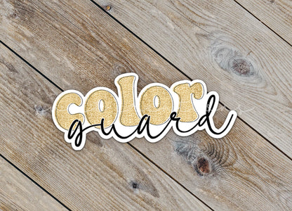 Close-up of the Gold Glitter Color Guard sticker on rustic wood