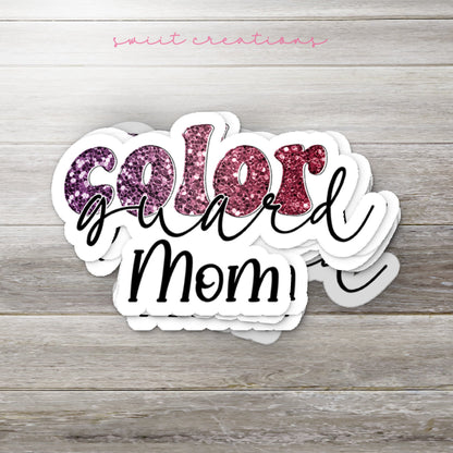 Stack of Maroon Glitter Color Guard Mom glossy stickers on a gray wood table