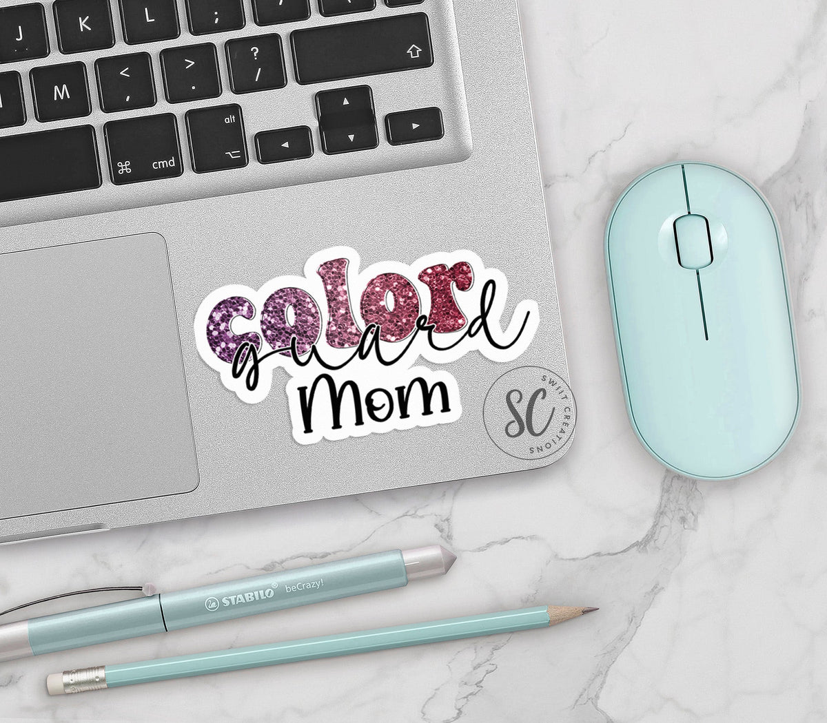 Maroon Glitter Color Guard Mom vinyl sticker on a silver laptop next to a mint mouse and pens