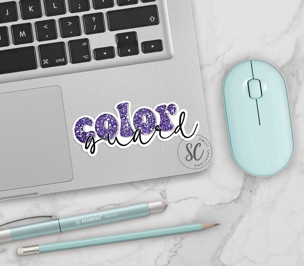 Purple Glitter Color Guard vinyl sticker on a silver laptop next to a mint mouse and pens
