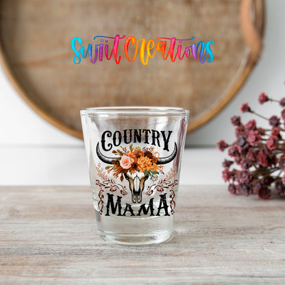 Country Mama shot glass transfer on a clear glass beside a wooden barrel and dried flowers