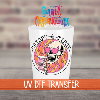Crispy and Tipsy UV DTF transfer on a white shot glass in front of a brick wall