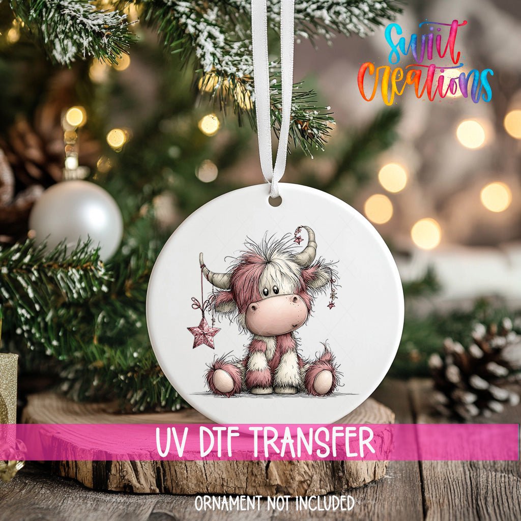 Pink Christmas Highland Cow ornament UV DTF transfer on an ornament resting on a wood slice beside a Christmas tree