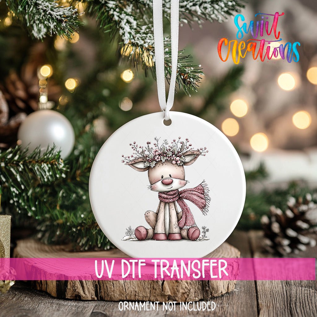 Pink Deer with Floral Crown ornament UV DTF transfer on an ornament resting on a wood slice beside a Christmas tree