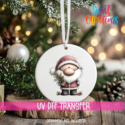 Santa with Pine Sprig ornament UV DTF transfer on an ornament resting on a wood slice beside a Christmas tree